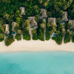 Aerial view of beachfront villas nestled among lush tropical greenery, each with private pools, along a pristine white sandy beach. The clear turquoise waters gently lap the shore, creating a serene and picturesque coastal scene, enhanced by Soneva Exclusive Offers for an unforgettable getaway.