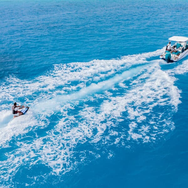 A person is being towed on a wakeboard by a boat in the clear blue ocean waters of the Maldives. The image captures the white waves created by the boat's movement and the bright, sunny weather. This Soneva exclusive experience conveys a sense of fun and adventure on the water.