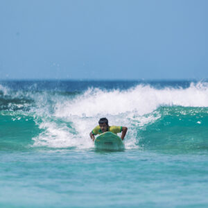 Person paddling on a surfboard towards an approaching wave in the middle of the ocean under a clear blue sky. Waves are breaking gently behind, with clear turquoise water all around. As they prepare to ride the wave, it’s reminiscent of Soneva exclusive offers blending adventure and serenity.