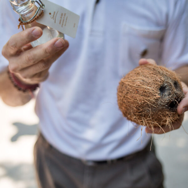 A person in a white shirt holding an unlabeled bottle in one hand and a coconut in the other, captures the essence of a Maldives Exclusive Experience. The background is slightly blurred, focusing on the items being held, echoing the luxury found at Soneva resorts. The person's face is not visible.