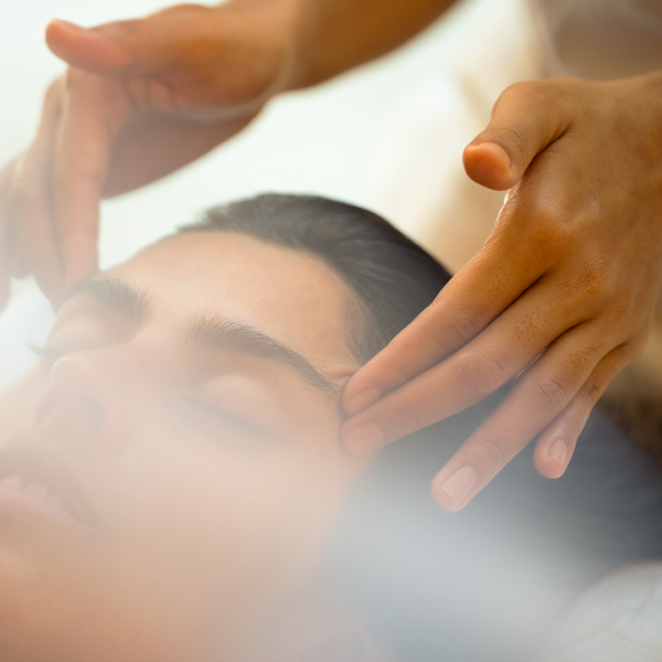 A person receives a facial massage, with close-up of hands gently pressing on the temples. The image is soft-focused, creating a serene and calming mood. The person's eyes are closed, clearly relaxed during the treatment, evoking the tranquility found in Soneva Exclusive Offers.