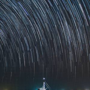 A long-exposure photo capturing a boat illuminated on the calm sea at Soneva in the Maldives under a night sky filled with dramatic star trails. The water reflects the light from the boat and the starry sky, enhancing this exclusive experience with its serene scene.